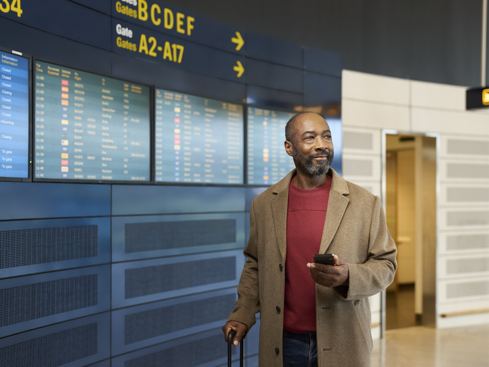 Traveler with a suitcase reading airport departure boards, still hearing clearly while his devices are repaired in Falconer, NY