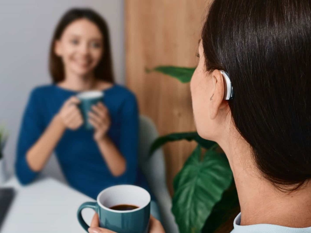 Woman wearing a receiver-in-canal hearing aid during a conversation over coffee, one of the styles fitted in Falconer, NY